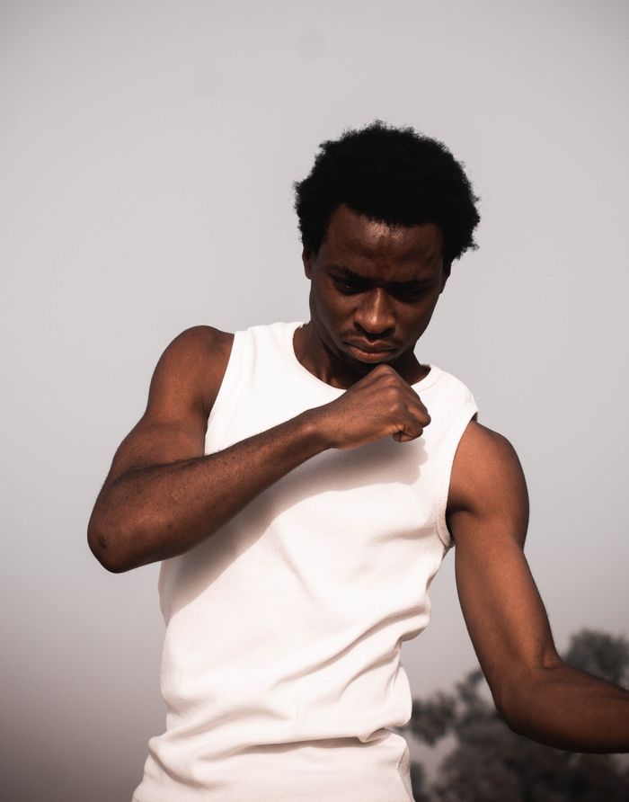 Portrait of a young man in a white tank top with thoughtful expression outdoors.